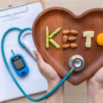 Hands holding a heart-shaped wooden plate with keto food arranged to spell 'KETO'