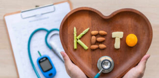 Hands holding a heart-shaped wooden plate with keto food arranged to spell 'KETO'