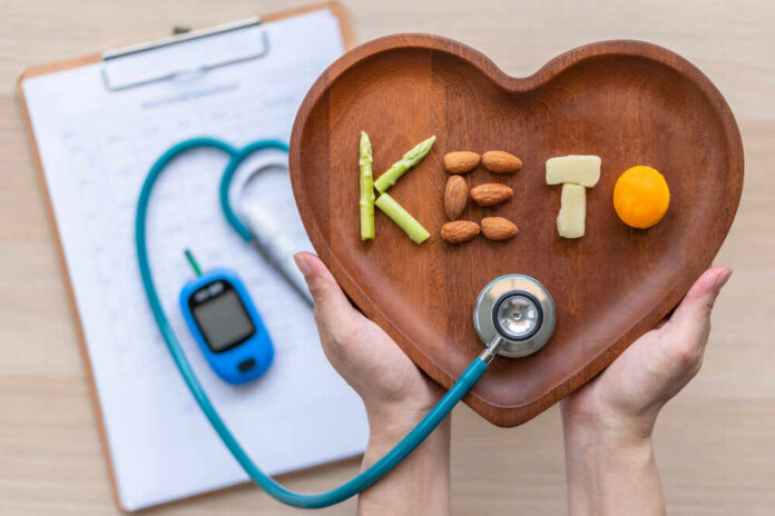 Hands holding a heart-shaped wooden plate with keto food arranged to spell 'KETO'