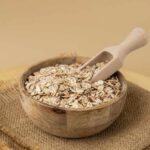 A wooden bowl filled with oats and a wooden scoop
