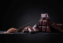 A pile of dark chocolate bars with cocoa powder on a black surface