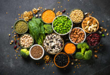 An assortment of legumes, nuts, and fresh vegetables arranged in bowls on a dark surface