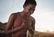 A woman in athletic wear holding her chest with a pained expression outdoors