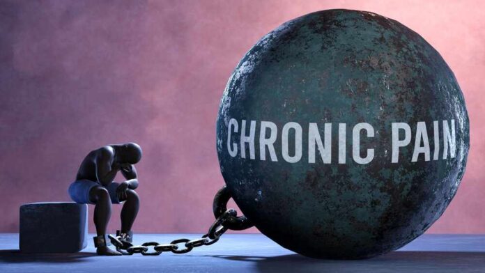 shutterstock_2261741371.jpg A figure representing chronic pain, sitting beside a large ball labeled 'CHRONIC PAIN' chained to their body