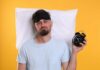 Sleep Study Reveals Surprising Success Formula Man wearing a sleep mask holding an alarm clock with a frustrated expression