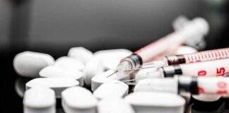 White pills and syringes arranged on a reflective surface