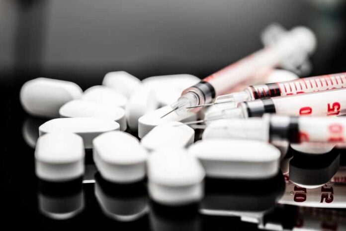 White pills and syringes arranged on a reflective surface