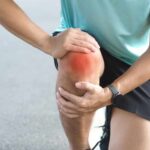 Athlete holding their knee in pain while exercising outdoors