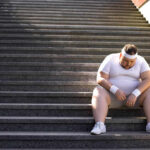 An exhausted man in sportswear sitting on outdoor stairs, looking down.
