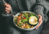 A person holding a bowl of colorful salad with avocado and greens