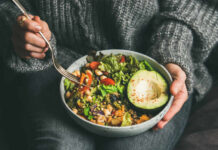A person holding a bowl of colorful salad with avocado and greens