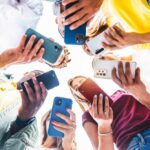A group of friends holding smartphones in a circle, looking down at their devices