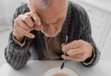 Elderly man focusing intently on a spoon while preparing to eat