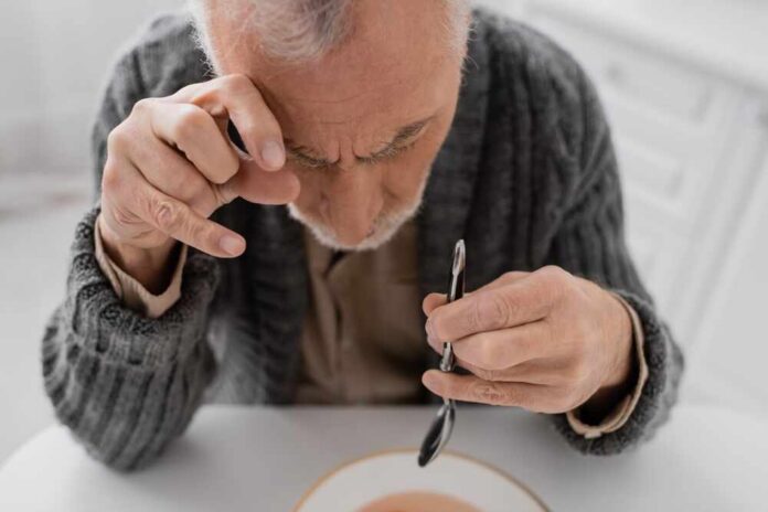 Elderly man focusing intently on a spoon while preparing to eat