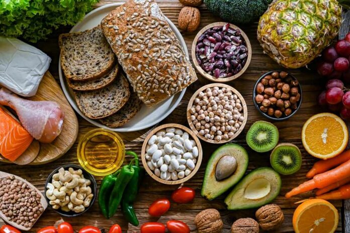 A variety of fresh foods including vegetables, fruits, grains, and proteins arranged on a wooden surface