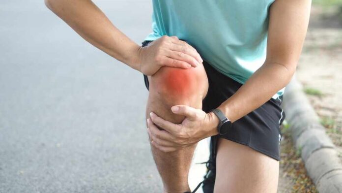 shutterstock_2563123695.jpg Athlete holding their knee in pain while exercising outdoors