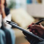 A therapist taking notes during a session with a client in the background