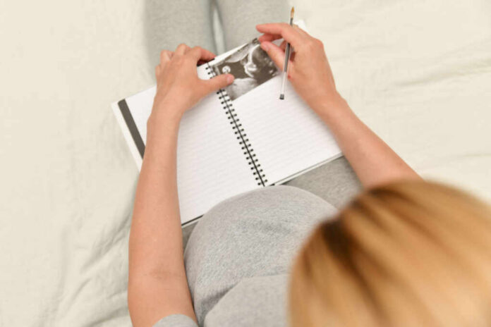 Pregnant woman writing in a journal while holding an ultrasound photo