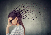 Estrogen’s Surprising Role in Your Brain Fog A woman with glasses holding her head, with fragments dispersing from her head