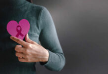 Person holding a pink heart with a ribbon symbol
