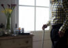 Elderly man standing with a cane next to a table with flowers and medication