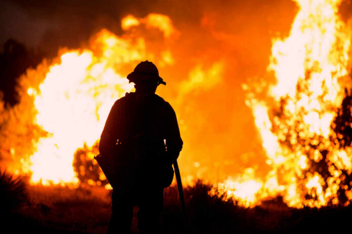 Silhouette of a firefighter standing in front of a large wildfire