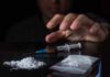 A hand reaching for a syringe next to a pile of white powder