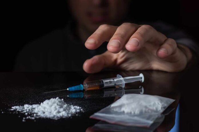 A hand reaching for a syringe next to a pile of white powder