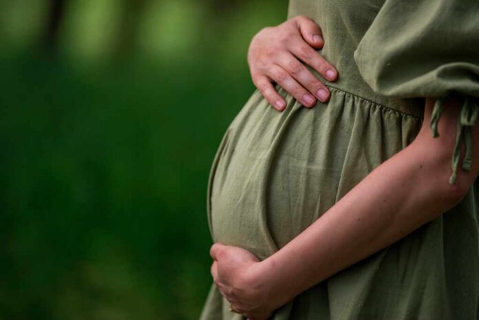 Caucasian,Young,Pregnant,Woman,Tummy,Belly,Summer,Green,Dress,Touching Pregnant woman in a green dress gently holding her belly in a natural setting