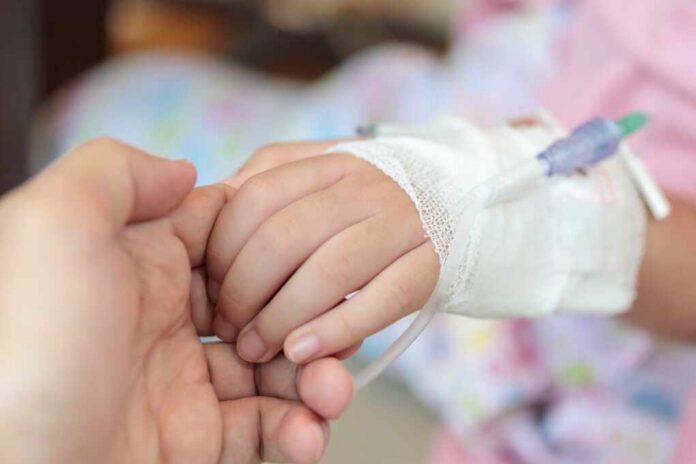 A childs hand with an IV drip being held by an adult hand