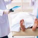 Medical staff stand near a covered body on a gurney with a toe tag