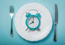 Fasting Earlier or Later in Day for Weight Loss? Alarm clock on a white plate with fork and knife