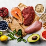 Assorted healthy foods with salmon, beef, chicken, fruits, vegetables, nuts, and grains