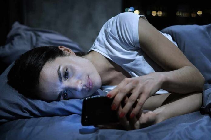 shutterstock_1208195308 Woman lying in bed looking at a smartphone