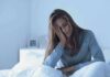 Bedtime Blunders Training Insomnia Woman sitting in bed with hand on face, looking tired