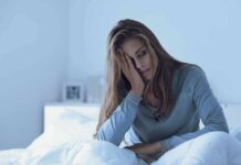 Bedtime Blunders Training Insomnia Woman sitting in bed with hand on face, looking tired