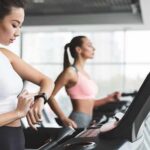 Woman on treadmill checking smartwatch in gym