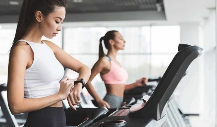 shutterstock_1403943743 Woman on treadmill checking smartwatch in gym