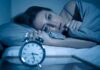 Scary Brain Shift Tied To Insomnia Woman lying awake in bed beside an alarm clock