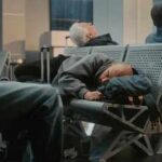 Passengers sleeping on airport benches with luggage nearby