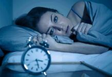 Why Women Are Hit Really Harder With Insomnia Woman lying awake in bed beside an alarm clock