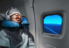 A passenger sleeping on an airplane with headphones and an eye mask