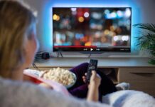 Person sitting on a couch watching a movie on a TV with popcorn in hand