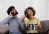 Your Home Is Sabotaging Your Brain Couple on couch reacting to ceiling leak as woman holds pot to catch water