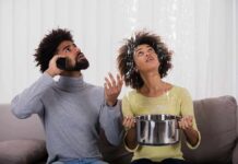Couple on couch reacting to ceiling leak as woman holds pot to catch water