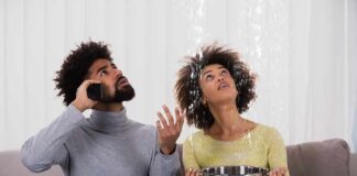 Couple on couch reacting to ceiling leak as woman holds pot to catch water