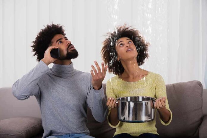 Couple on couch reacting to ceiling leak as woman holds pot to catch water