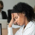 Woman in office holding her head with eyes closed