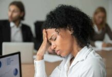 Woman in office holding her head with eyes closed