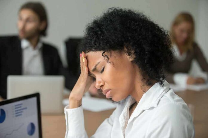 Woman in office holding her head with eyes closed